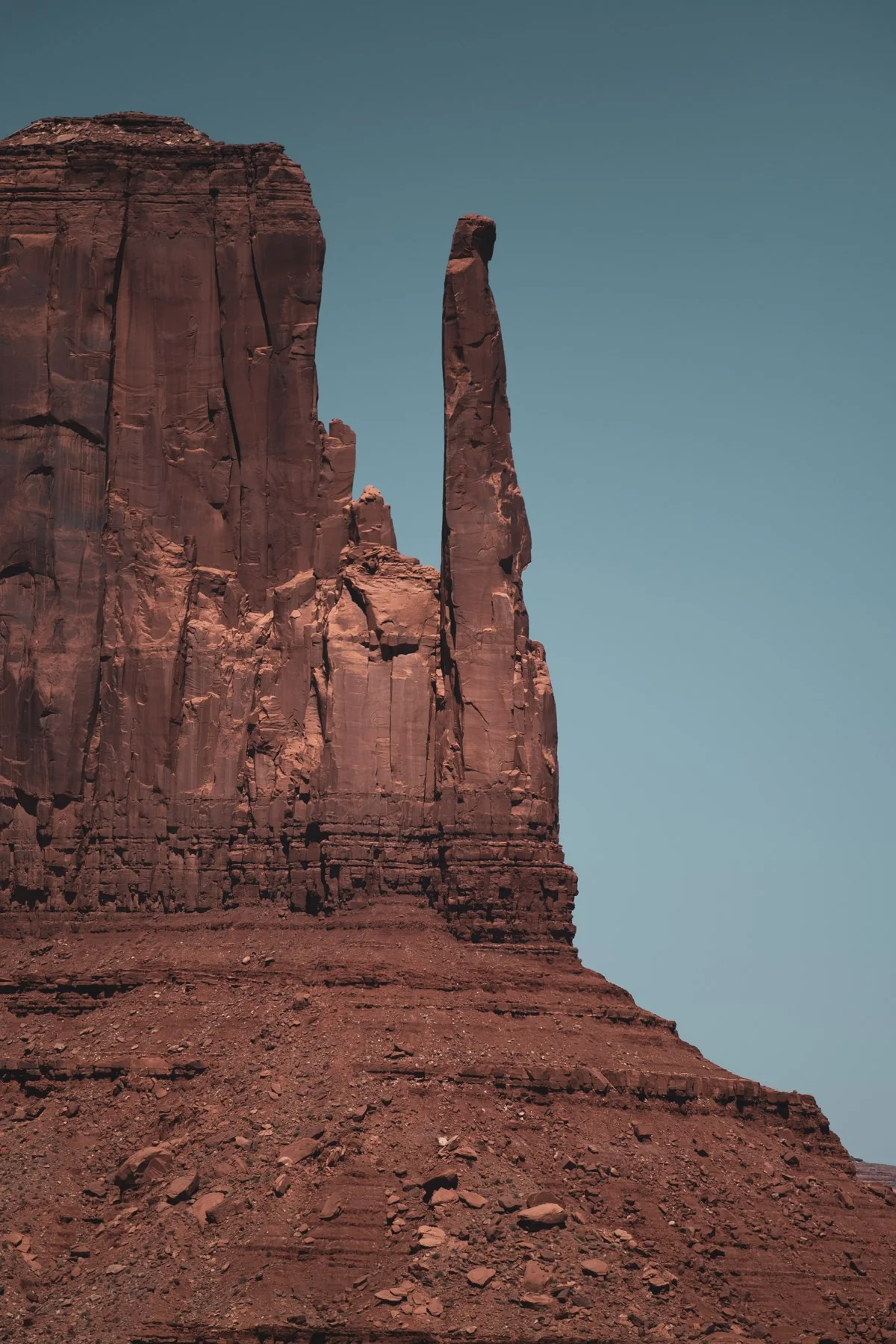 A narrow sandstone spire beside a red-rock butte in Monument Valley