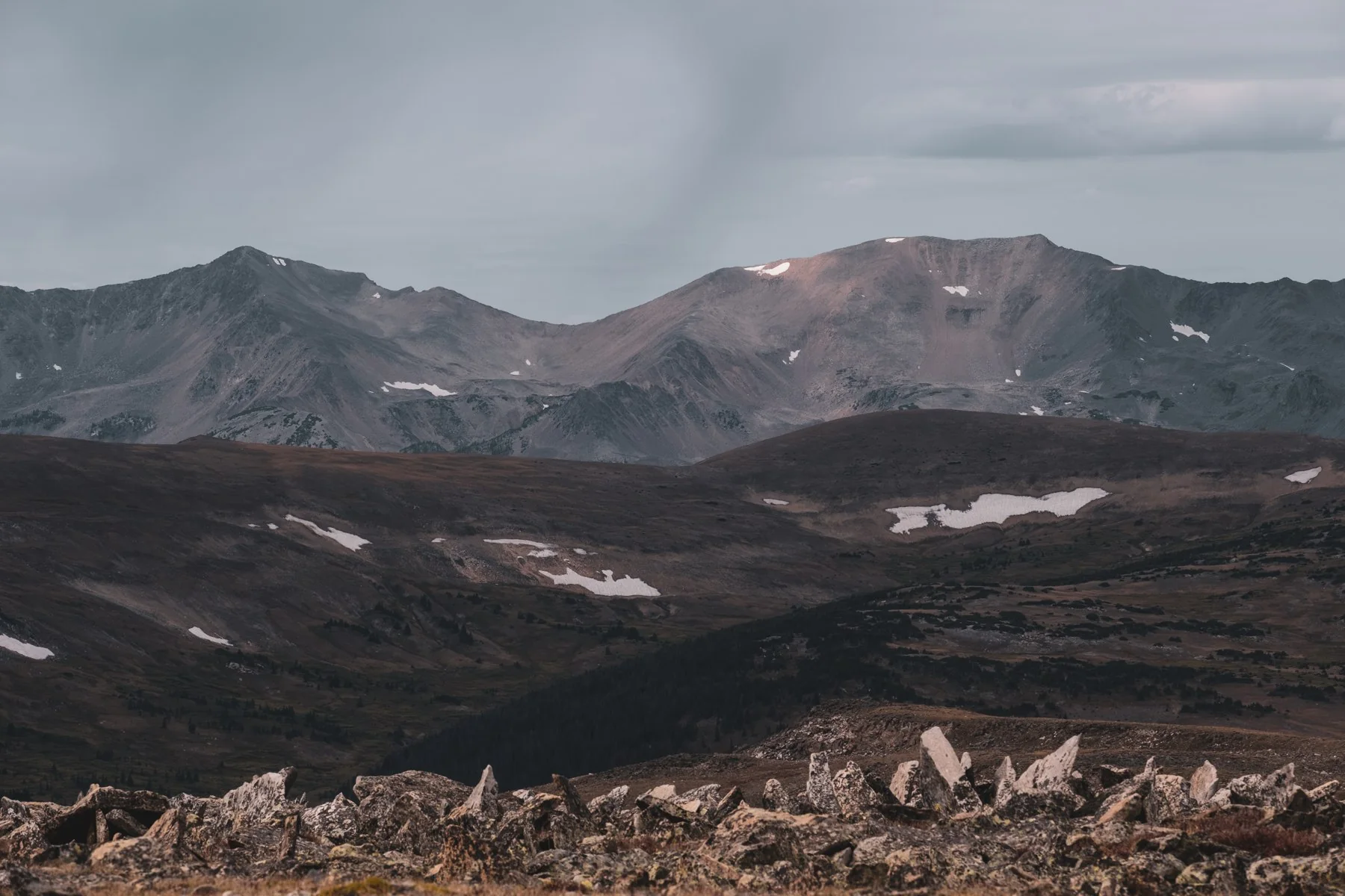Mountain ridges and patches of snow under a cloudy sky in Colorado